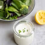 Homemade ranch dressing in a glass jar with a salad and a half of lemon in the background.