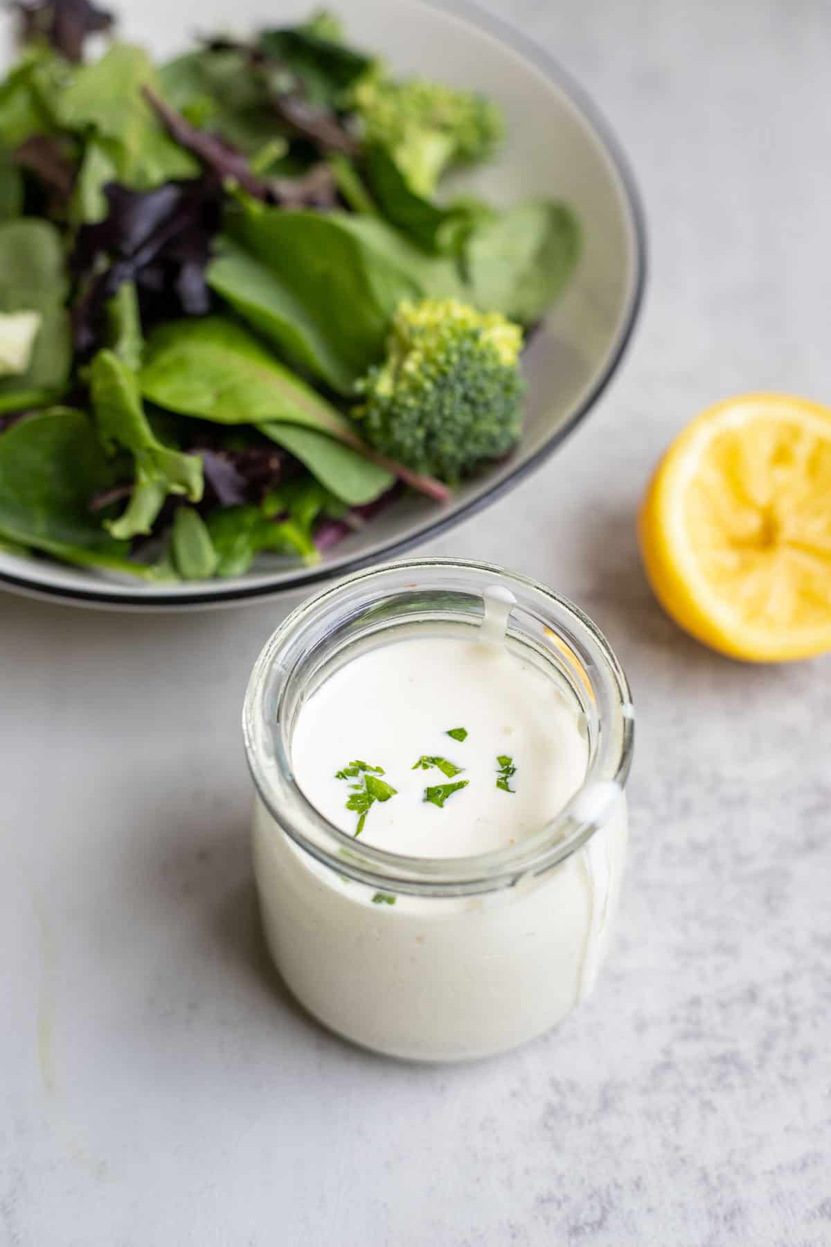 Homemade ranch dressing in a glass jar with a salad and a half of lemon in the background.