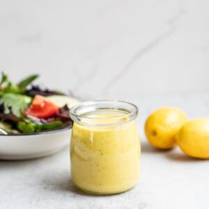 Honey mustard dressing in a glass jar with lemons and a salad in a bowl in the background.