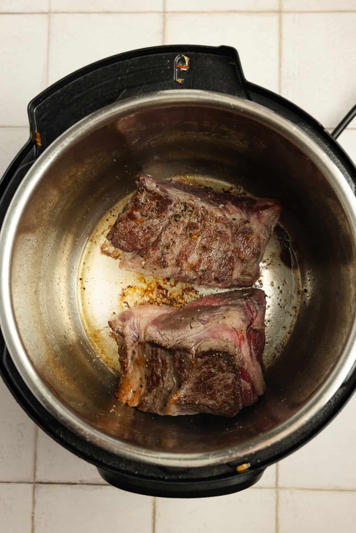 Two pieces of beef browning in an instant pot.