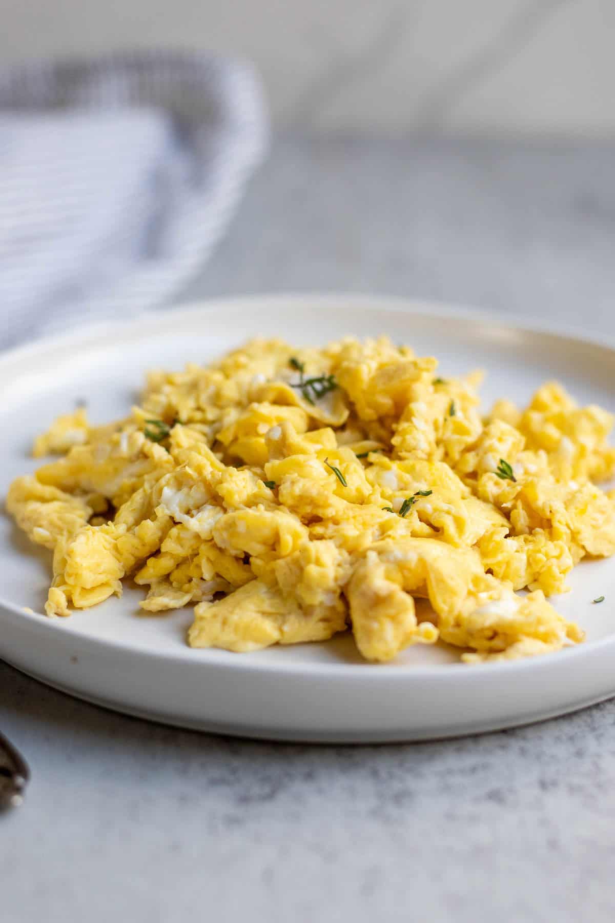 Scrambled eggs topped with fresh thyme on a white plate.