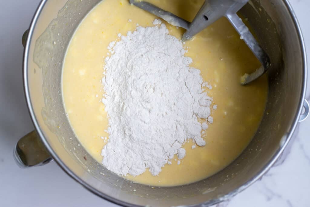 Adding flour a little bit at a time to the wet ingredients in a stand mixer bowl.
