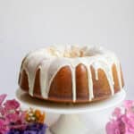 Sourdough bundt cake with icing on a white cake stand surrounded by flours.