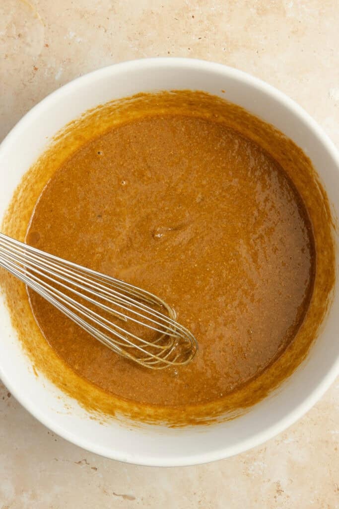 Wet ingredients added to a bowl with a whisk in it.