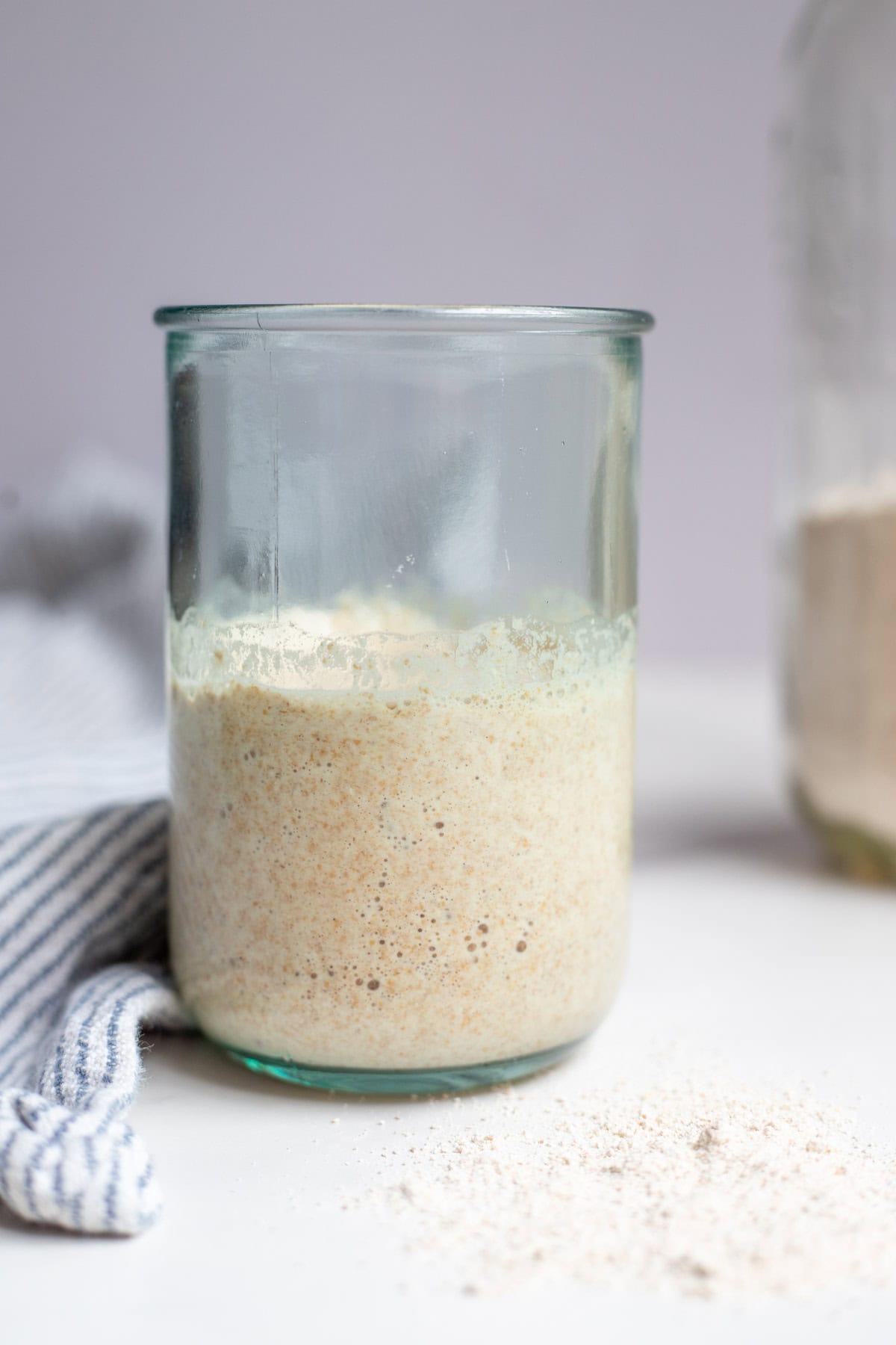 Spelt sourdough starter in a glass jar with a towel on a white countertop.