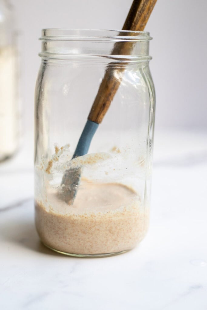 Spelt starter in a jar with a wooden spatula.