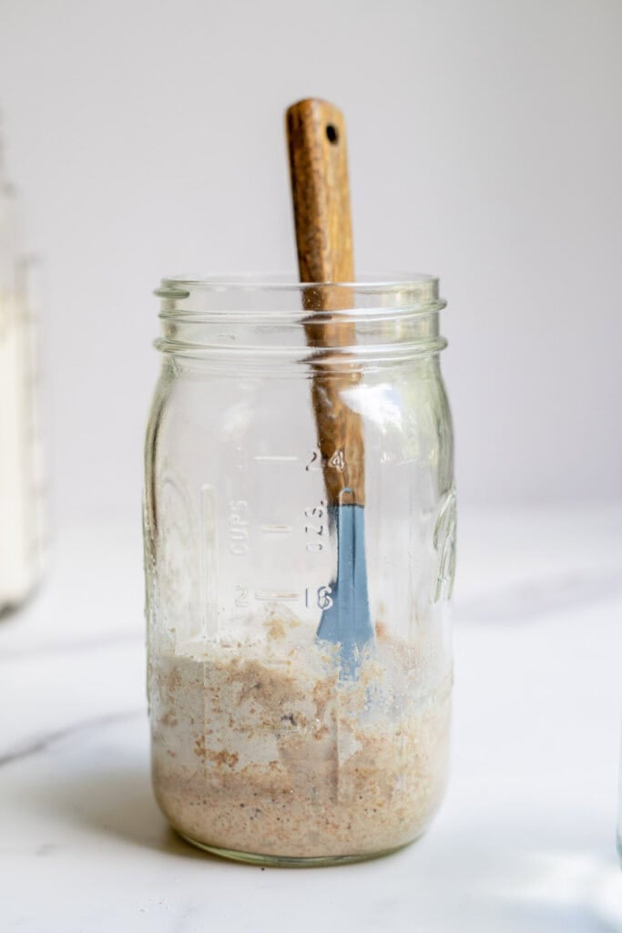Adding spelt flour and water to a jar with sourdough starter.