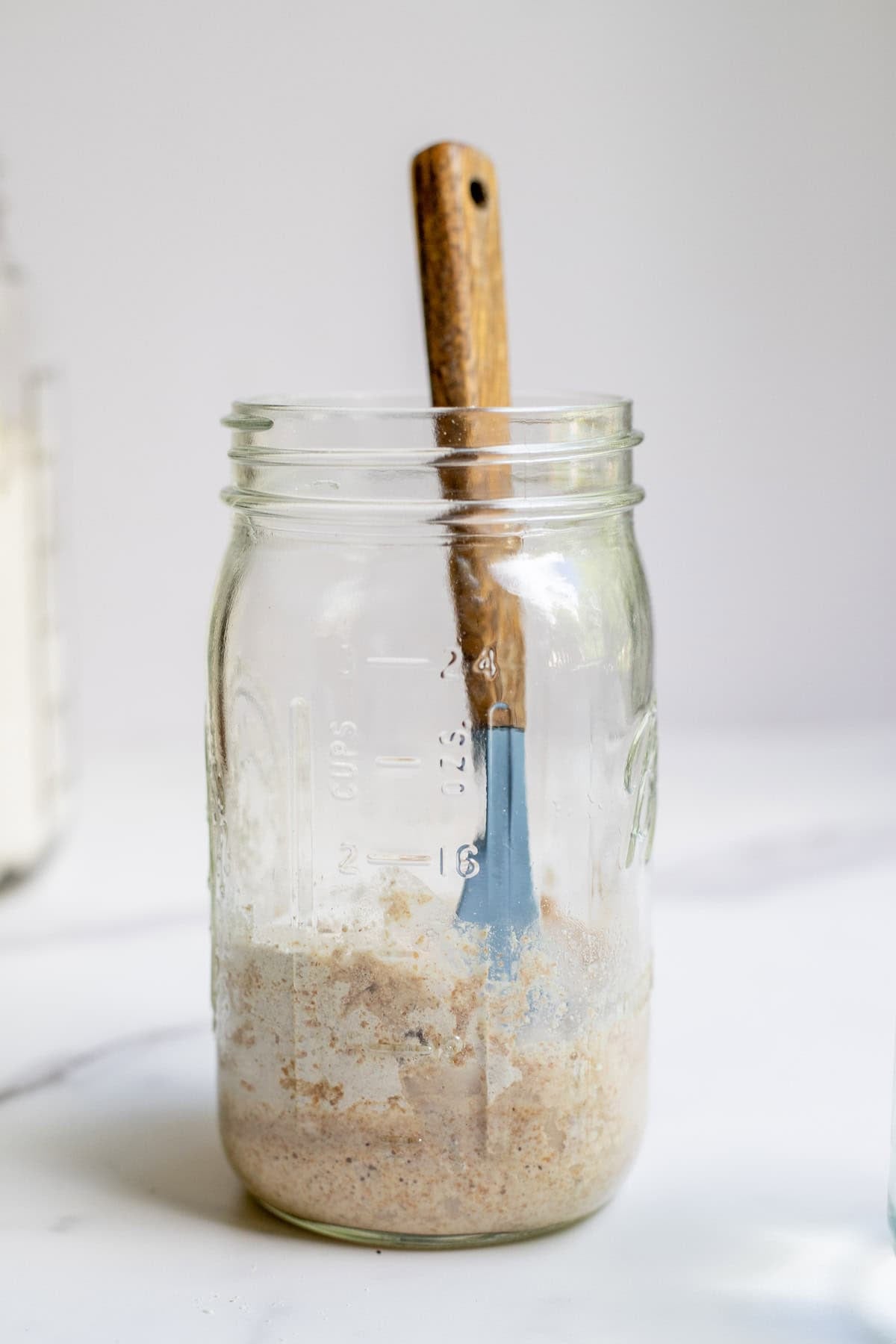 Adding spelt flour and water to a jar with sourdough starter.