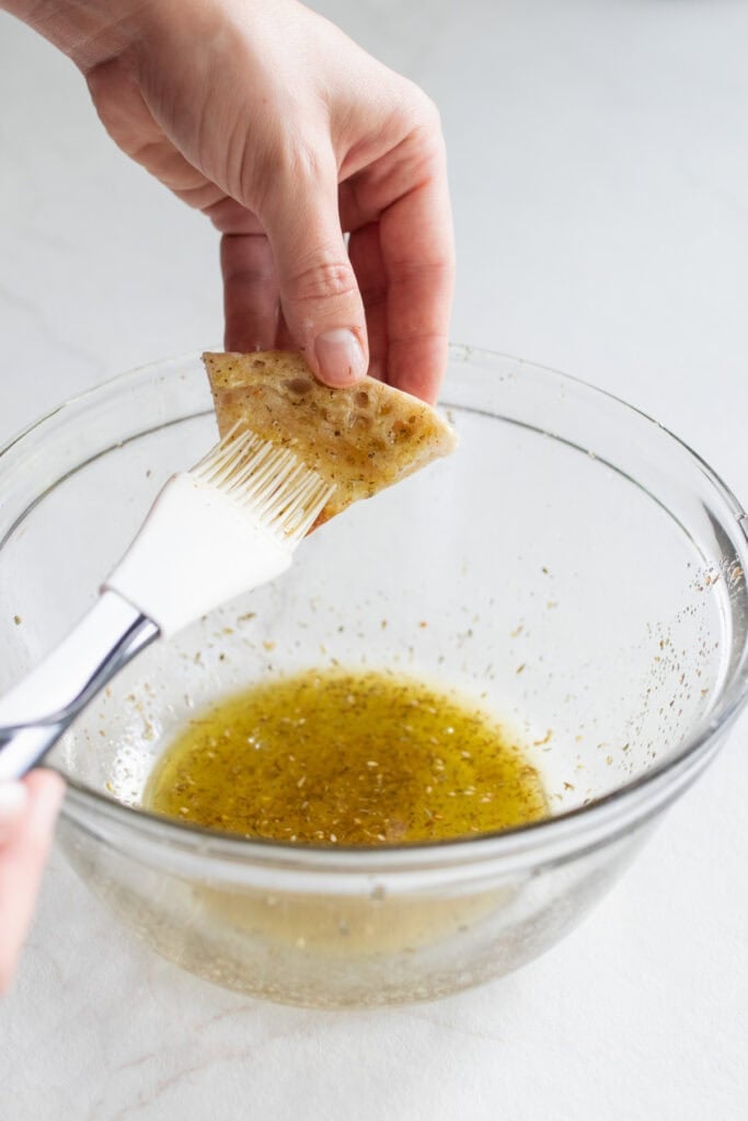 A triangle of pita bread being brushed in a olive oil mixture.