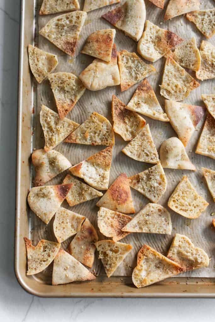 Pita bread triangles baking on a baking sheet.