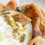 pita chips layered around a bowl of white dip.