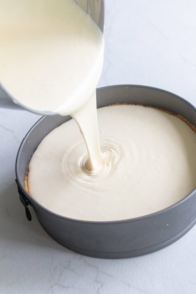 Cheesecake batter being poured into a metal pan.