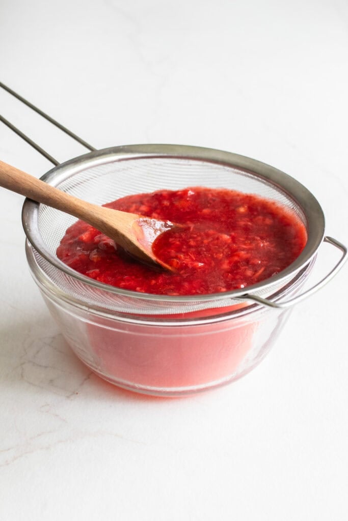 Strawberry sauce being strained through a mesh sieve.
