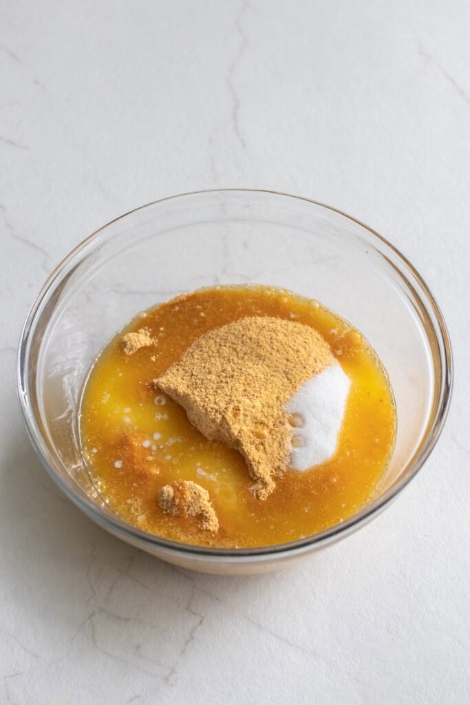 Ground graham crackers and melted butter in a glass bowl.