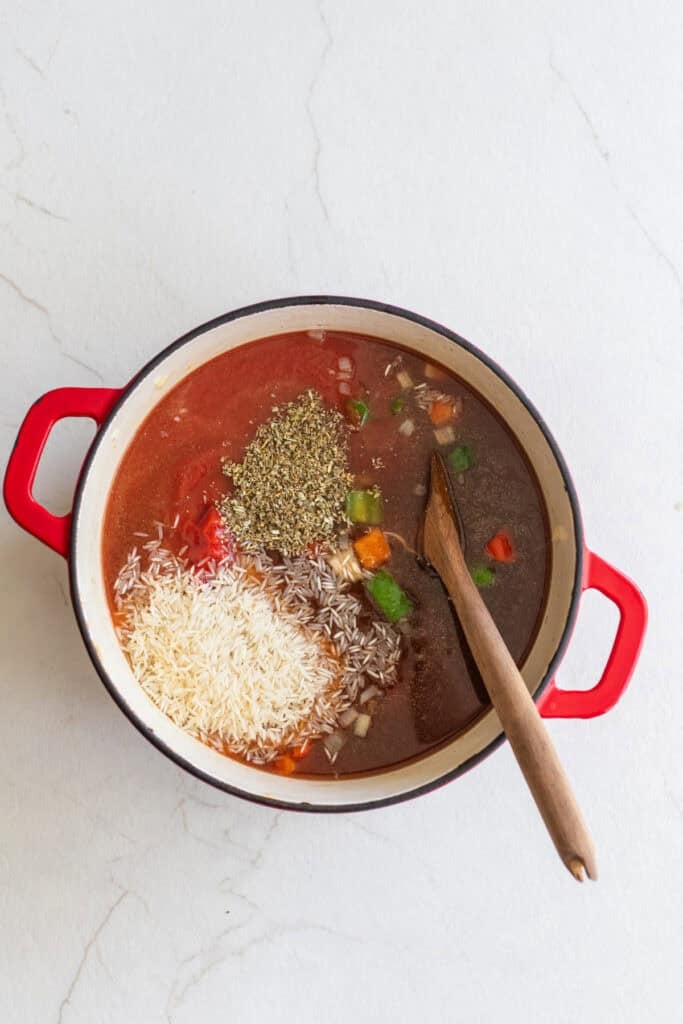 A pot full of rice, bell peppers, rice, dried herbs, and diced tomatoes.