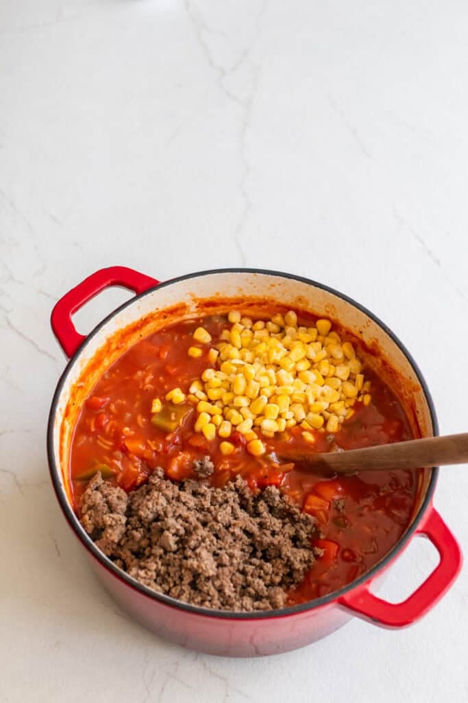 A full pot of soup with ground beef and corn kernels added.
