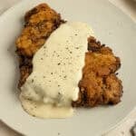 Chicken fried steak topped with gravy on a white plate.