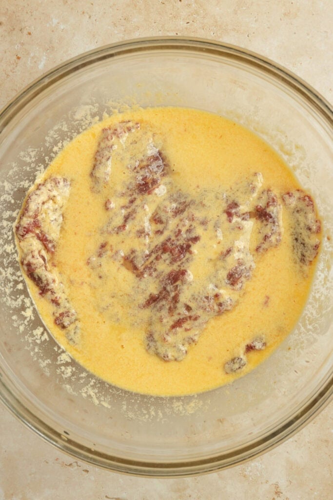 Egg mixture and cube steak in a glass bowl.