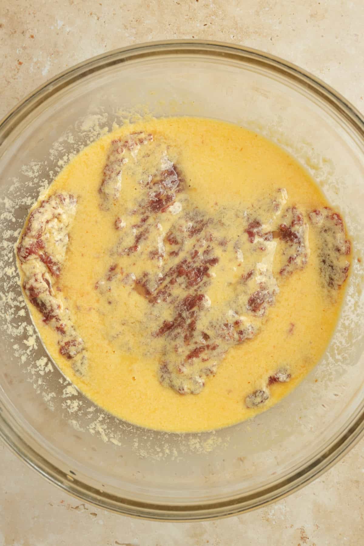Egg mixture and cube steak in a glass bowl.