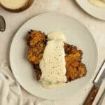 Chicken fried steak covered with white gravy on a white plate.