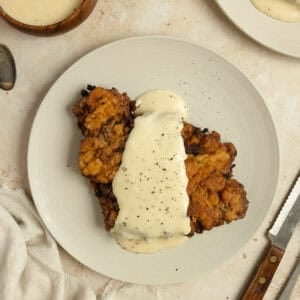 Chicken fried steak covered with white gravy on a white plate.