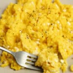 scrambled eggs on a plate with a silver fork.