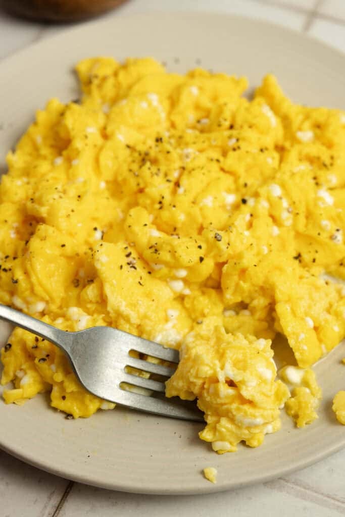 Finished scrambled eggs on a plate with a fork. 