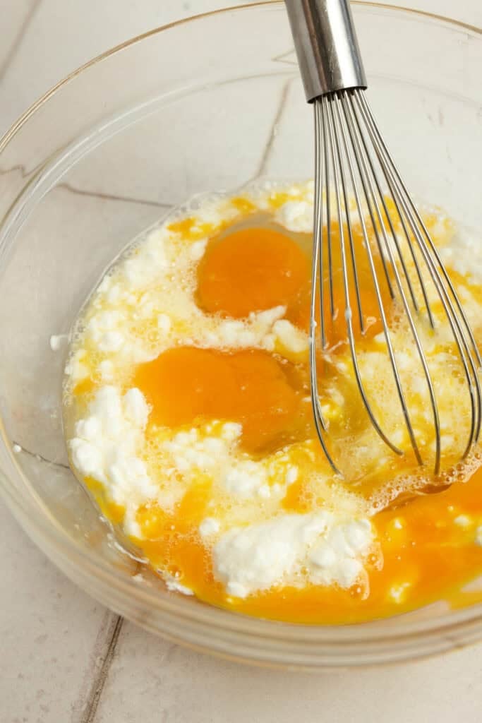 Eggs and cottage cheese being whisked together in a glass bowl.