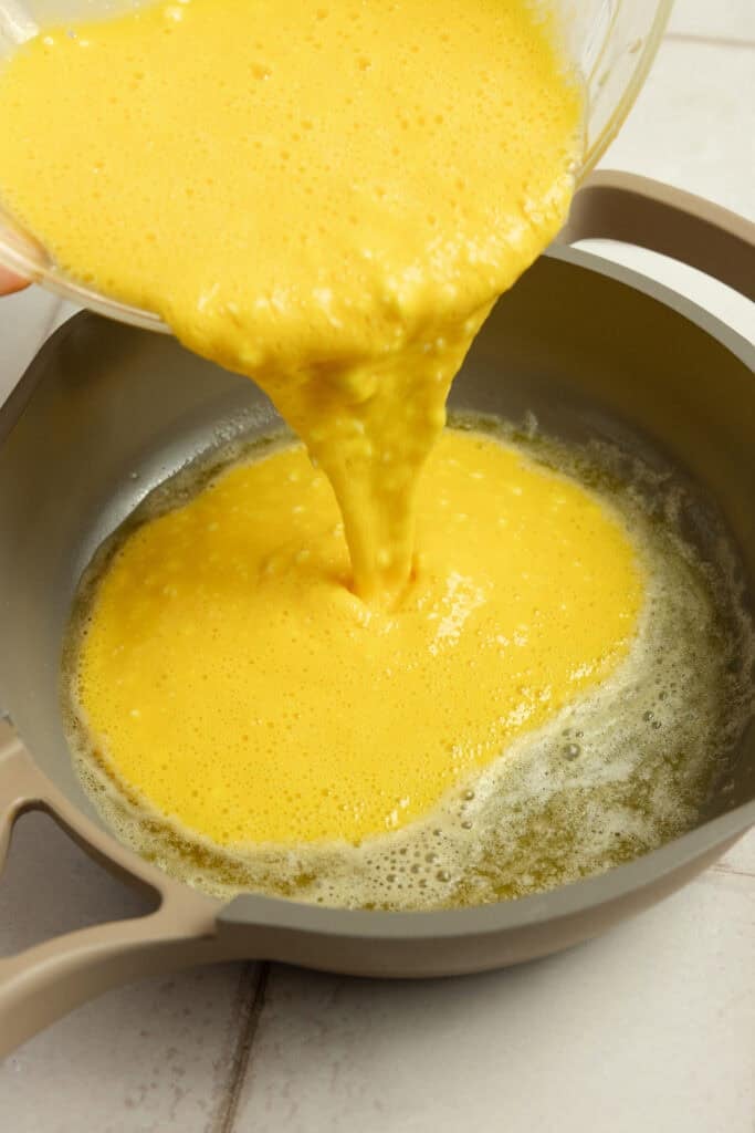 Scrambled egg mixture being poured into a hot skillet on the stove.