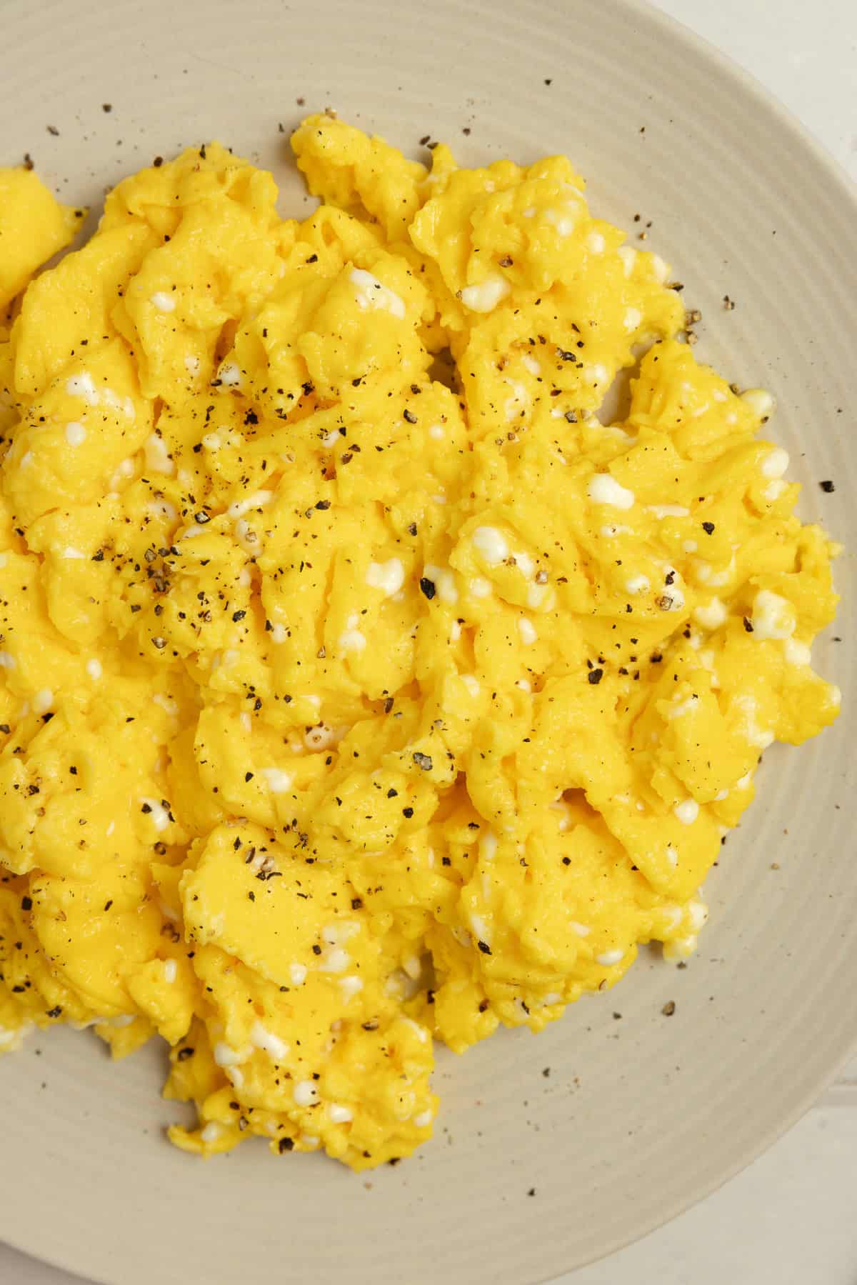 Scrambled eggs on an off white colored plate.