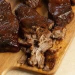 Country style ribs covered in barbecue sauce on a wood cutting board.