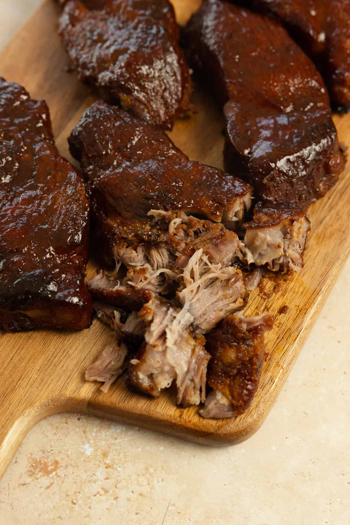 Country style ribs covered in barbecue sauce on a wood cutting board.