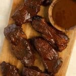 Country style ribs on a wood cutting board with more barbecue sauce in a bowl.