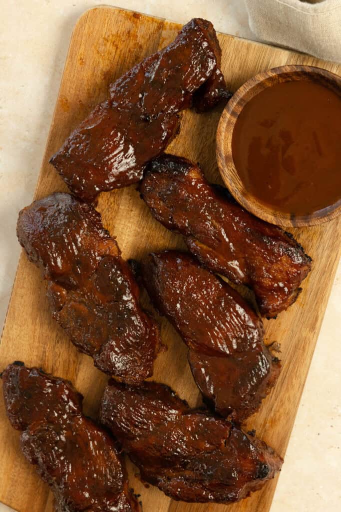 Country style ribs on a wood cutting board with more barbecue sauce in a bowl.