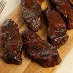 Country style pork ribs covered in barbecue sauce on a wooden cutting board.