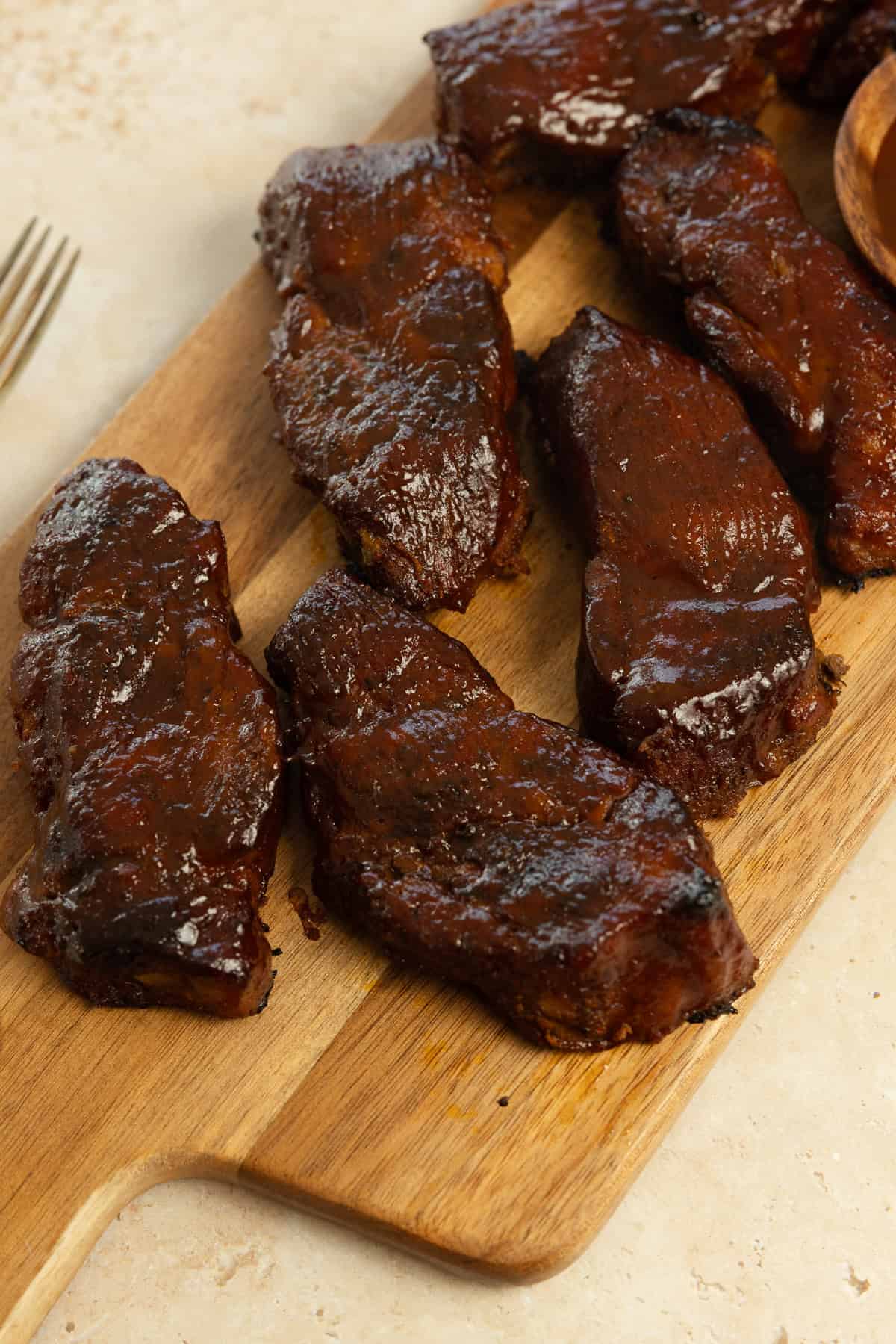 Country style pork ribs covered in barbecue sauce on a wooden cutting board.