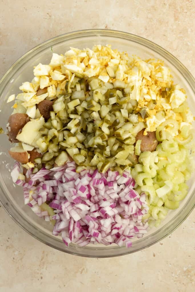 Adding pickles, onions, and other ingredients to cooked potatoes.