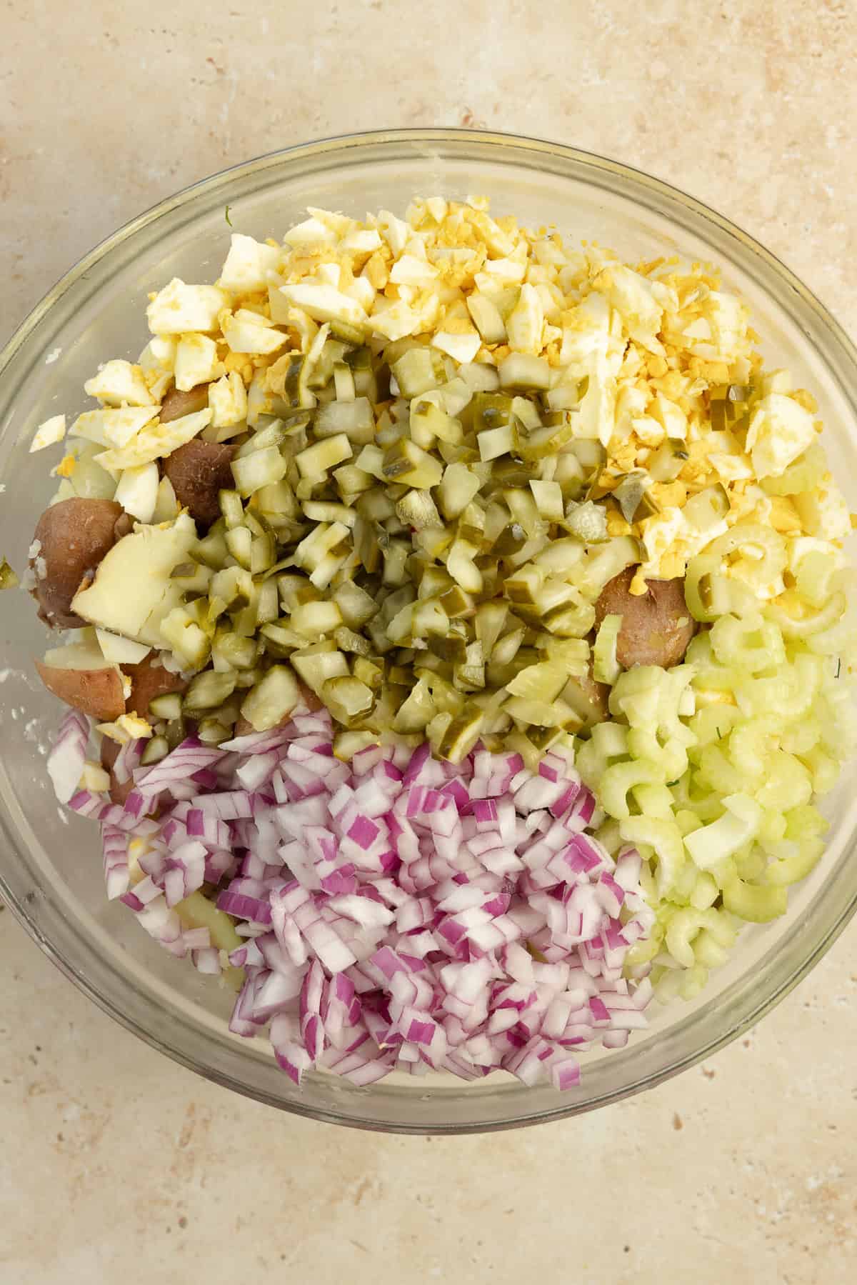 Adding pickles, onions, and other ingredients to cooked potatoes.