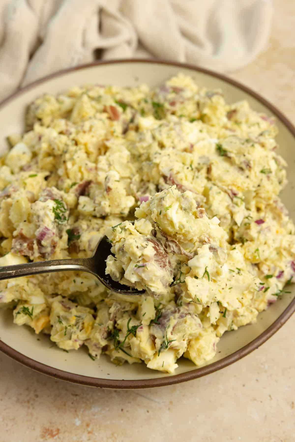 Scooping out a spoonful of dill potato salad in a bowl.