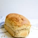 Loaf of fresh milled sourdough sandwich bread on a countertop surrounded by wheat berries.