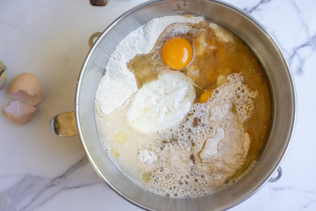 Overhead photo of whole wheat flour, eggs, water, oil, sourdough starter and salt in a stand mixer bowl.