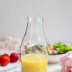 Homemade poppy seed salad dressing in a glass bottle with a salad and strawberries in the background.