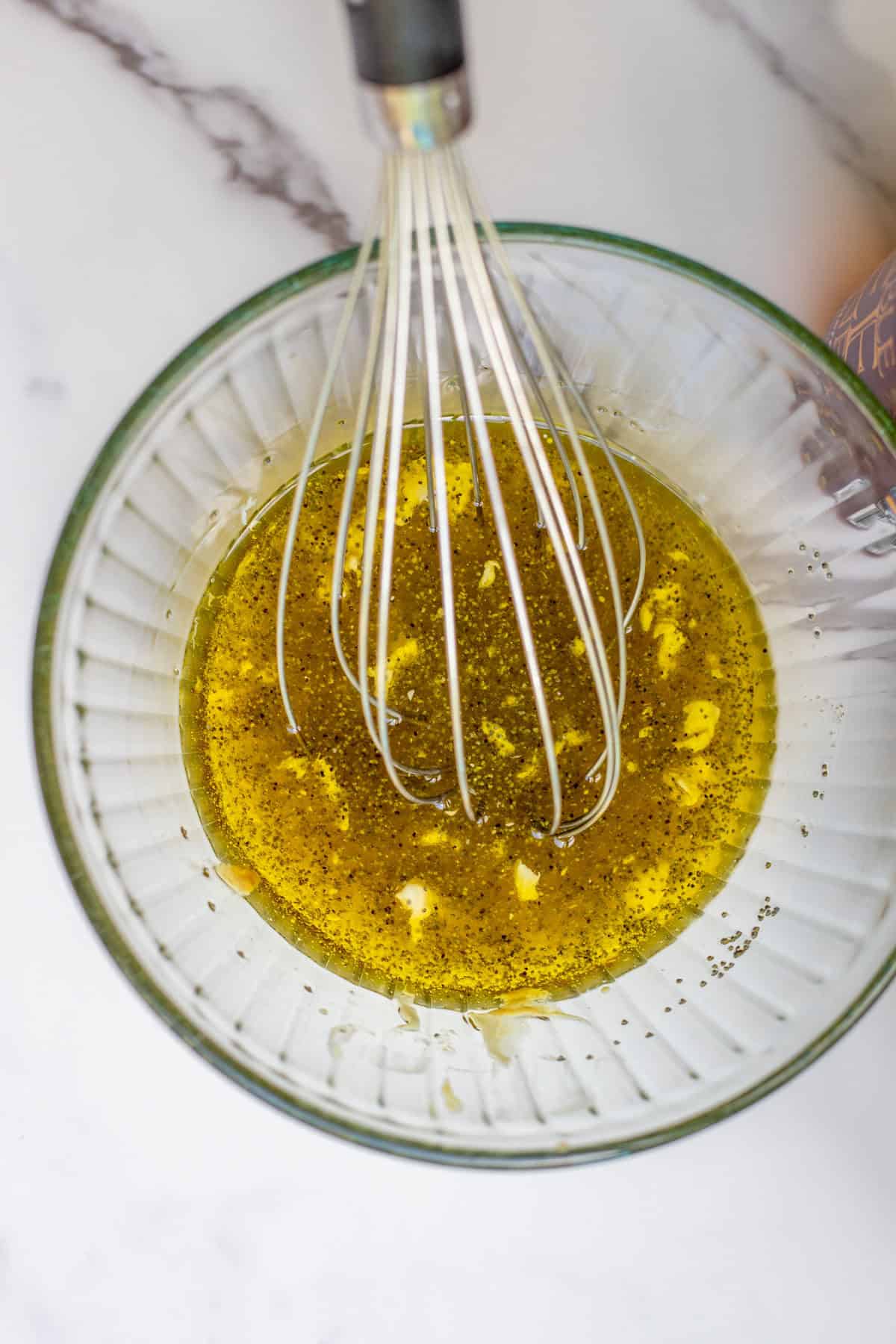 Olive oil, mayo, poppy seeds, honey and other ingredients in a bowl with a whisk.