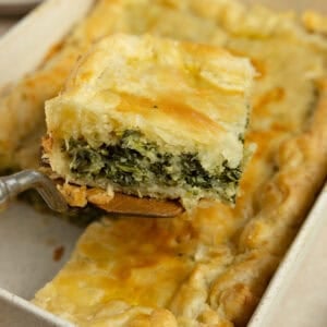 A square piece of spinach pie being served from a baking dish.