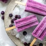 three blueberry popsicles resting on a tray of ice.
