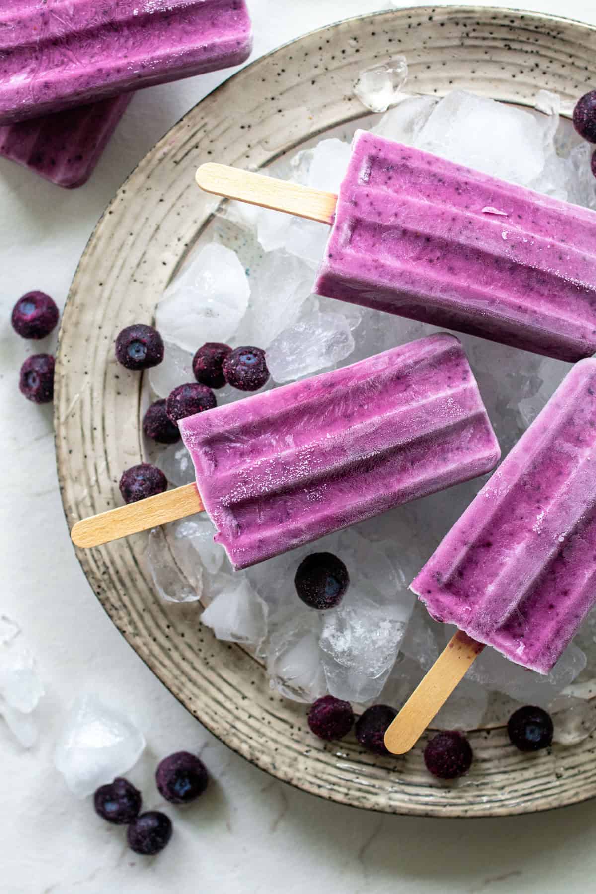 Three blueberry popsicles resting on a tray of ice.