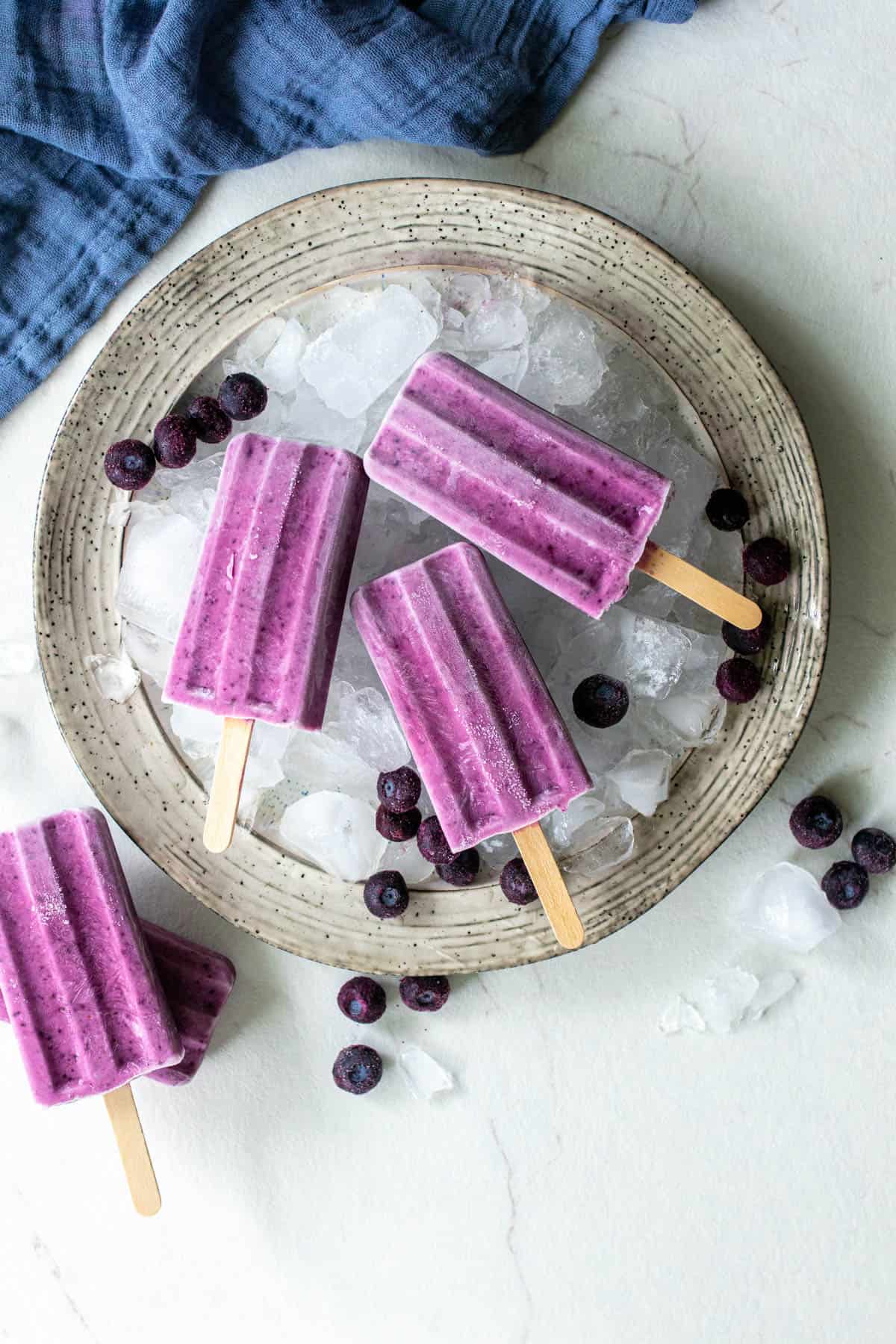 Four blueberry popsicles sitting in a tray of ice.