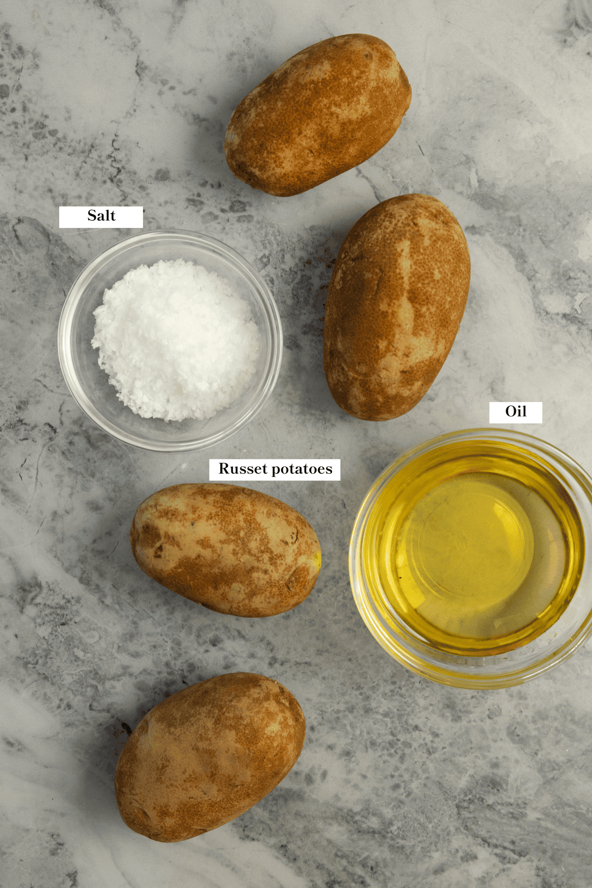 Potatoes, oil, and salt sitting on a marble countertop.