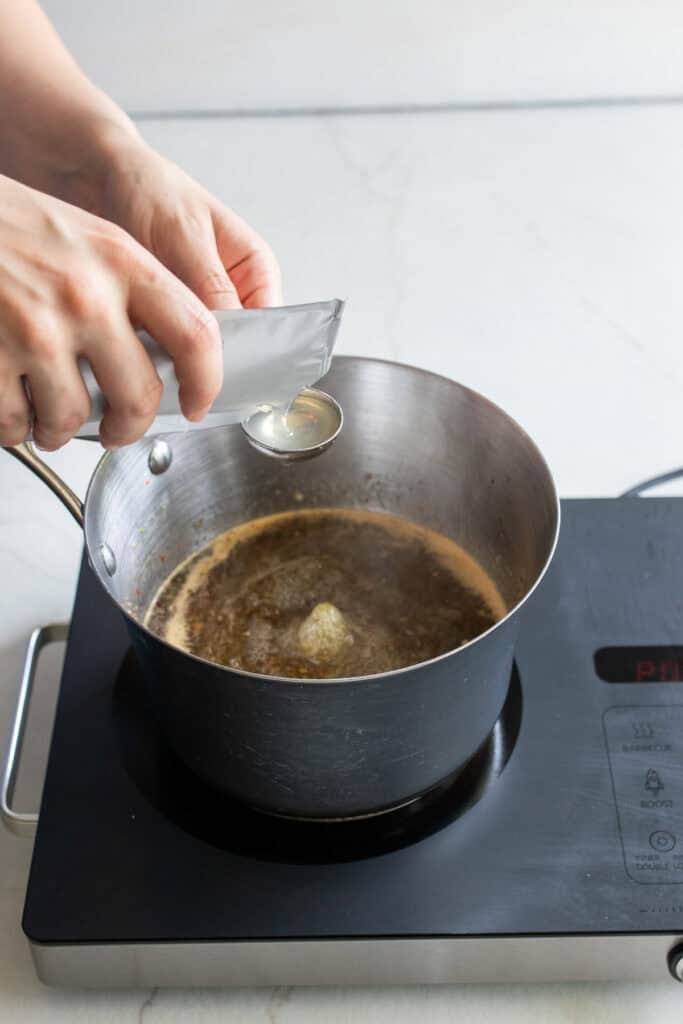 Adding liquid pectin to a large pot of pepper jelly.