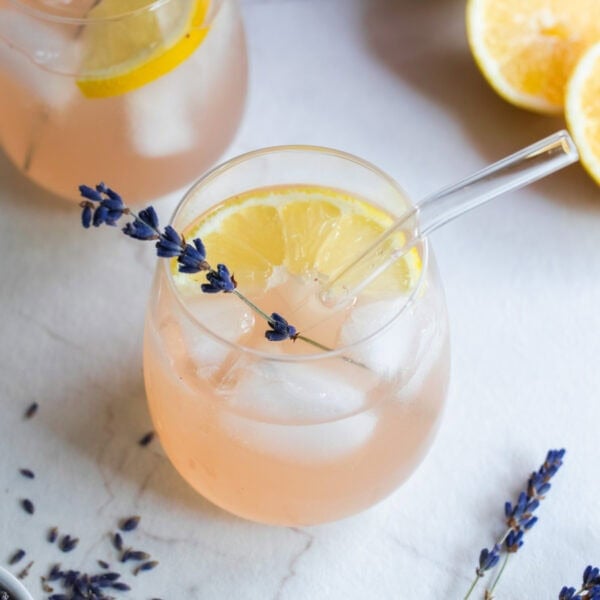 a glass of lemonade with a sprig of lavender and diced lemons in the glass.